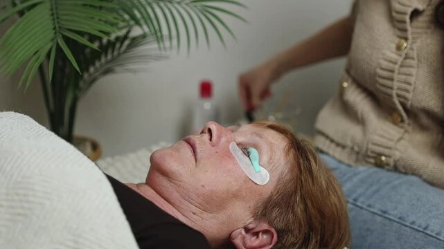 A young girl cosmetologist laminates the eyelashes of a senior woman.