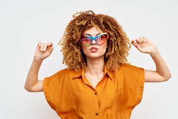 Stylish woman with curly hair wearing colorful oversized sunglasses, posing confidently against a plain white background, showcasing a vibrant summer look