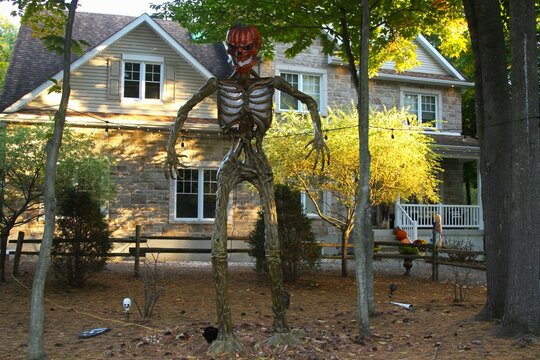 Tall outdoor skeleton body sculpture with pumpkin shape head.