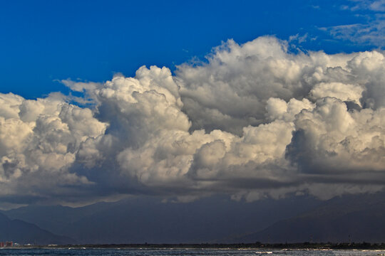 view of the horizon from Indaia beach, with a large white cumulus cloud covering the Serra do Mar mountains.
