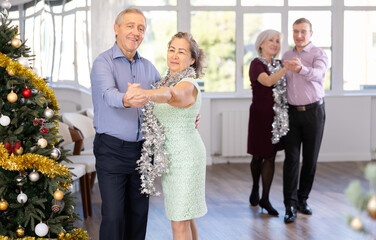 Aged man engaged in dance hall with mature female partner and dances Latin rumba during celebration...