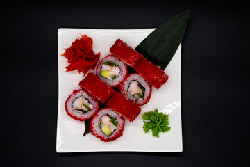 Prepared sushi rolls on a white plate on a black background