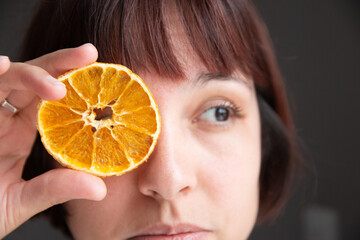 Mujer sostiene una rebanada de naranja frente a su cara