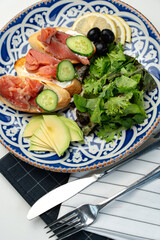 Colorful plate of smoked salmon sandwiches with cucumbers, greens, and olives on a decorative blue platter