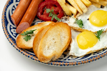 Breakfast plate with fried eggs, sausage, tomatoes, and fries served on a decorative blue plate
