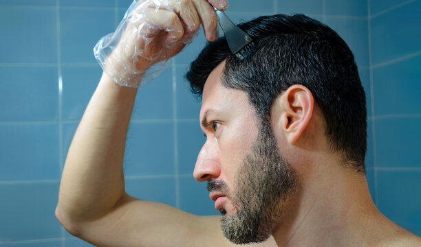 Hombre ti&ntilde;endo su cabello con cepillo, brocha y guante para cubrir sus canas. Aplicaci&oacute;n de tinte en casa. 