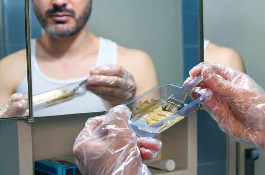 Hombre mezclando tinte para te&ntilde;ir su barba y bigote, usando cepillo y guantes de pl&aacute;stico. 