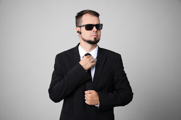 Young bodyguard in suit and sunglasses on grey background