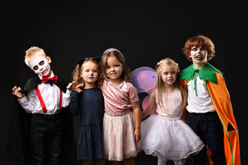 Funny children wearing costumes for Halloween celebration on black background