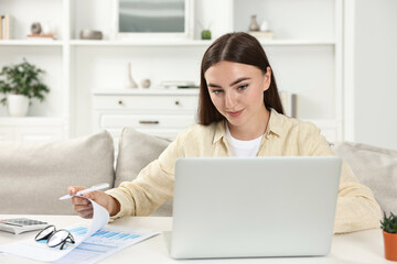 Obraz premium Budget planning. Young woman with papers using laptop at white table indoors