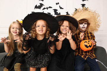 Cute children with pumpkin bucket wearing costumes indoors. Halloween celebration