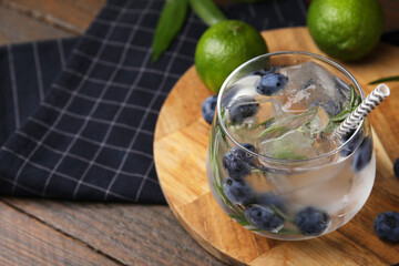 Refreshing water with blueberries and rosemary in glass on wooden table, closeup. Space for text