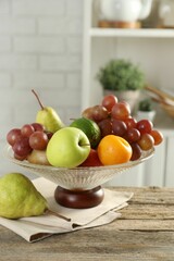Glass vase with different fresh fruits on wooden table