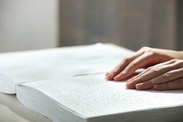 Blind woman reading book written in Braille at wooden table, closeup
