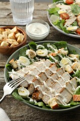 Delicious Caesar salad with chicken on wooden table, closeup