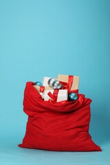 Santa Claus bag with baubles and gift boxes on light blue background