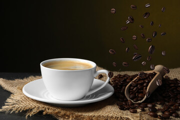 Cup of aromatic coffee and falling roasted beans on table