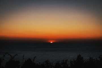 El último rayo de sol se despide en el horizonte, mientras el cielo y el mar se tiñen de tonos...