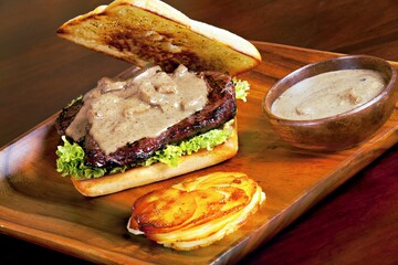 A delicious sandwich with steak, lettuce, and creamy sauce, served with a side.