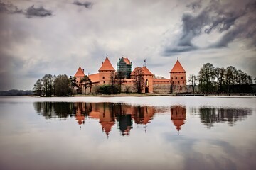 Fototapeta premium A picturesque castle reflecting in calm waters under a cloudy sky.