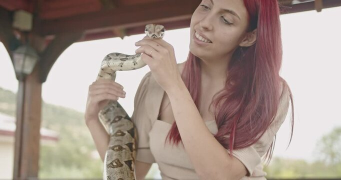 A happy young woman interacts playfully with her pet snake at an outdoor gazebo.