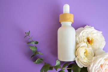 Flat lay of a white dropper bottle with wooden cap on a purple background and florals