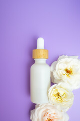 Flat lay of a white dropper bottle with wooden cap on a purple background and florals