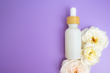 Flat lay of a white dropper bottle with wooden cap on a purple background and florals