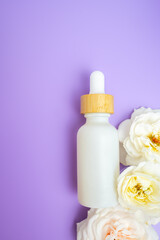 Flat lay of a white dropper bottle with wooden cap on a purple background and florals