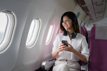 Fototapeta premium Business Woman Traveling in Business Class on a Plane, Using Smartphone and Headphones, Enjoying Comfortable Flight