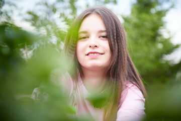 Portrait of young pretty woman with long brown hair in greenery