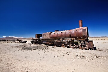 An abandoned rusted steam locomotive in a desolate landscape under a clear blue sky.