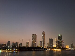 Nighttime scene of tall buildings adorned with lights by the riverside. Perfect for use as an illustration element or as a background