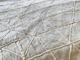 A closeup of intricate off-white geometric pintucks on cotton fabric reveals a finely textured surface, exuding a refined and minimalistic charm. 