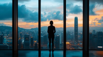 Fototapeta premium A person standing at a large window, looking out at a city skyline, thinking about the future and career goals