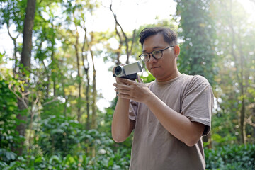 Young Asian man behind the camera directs and shoots the scene, video production enthusiast uses...
