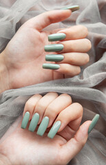 Elegant green manicure displayed on softly draped fabric with hands positioned artistically