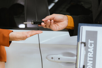 A businessman and his customer agree to a lease on a luxury car. The salesperson hands over the car keys as the customer signs a digital contract on a tablet to successfully close the sale.