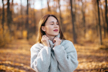 A woman with dark hair, wearing a gray sweater and a black floral print skirt, is in an autumn forest.