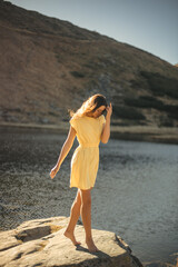 Serene Young Woman in Yellow Dress Enjoying a Walk by the Lake in Sunshine