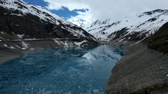 4k Drone Aerial Slow Shot Of Vibrant Blue Glacial Water Of Lac de Moiry Dam Surrounded By Massive Snow Covered Mountains Reflecting On lake In Grimentz Switzerland