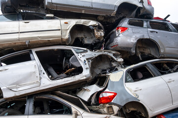 A junkyard filled with a large pile of abandoned and damaged cars stacked on top of each other, in...