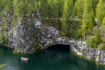 Visitors canoe across the tranquil waters of Marble Canyon, surrounded by lush greenery and stunning rock formations in Karelia