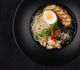 Steaming bowl of chicken ramen on black table setting