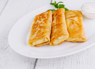 Thin pancakes with filling lying on white plate on wooden table