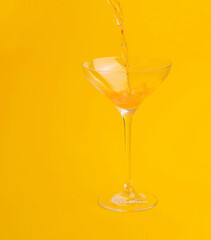Orange juice pouring into a glass on a yellow background
