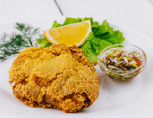 Breaded fish fillet served on white plate with lemon and sauce