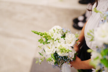 A beautiful white and blue bouquet in the hands of a schoolboy on the first of September. In the background, schoolchildren are out of focus.
