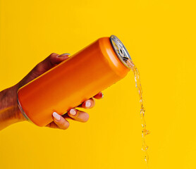 Woman holding spilling orange aluminum can on yellow background