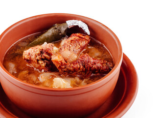 Steaming hot soup with meat and potatoes served in a clay pot on a plate